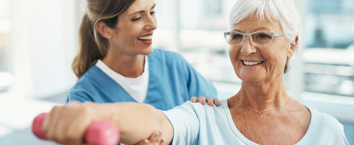 Older woman lifting weight with physical therapist helping