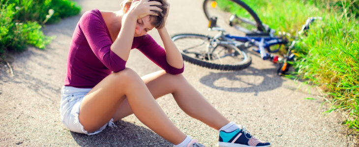 Woman who has fallen off a bicycle holding her head with a concussion